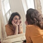 woman smiling wide at her reflection in the mirror