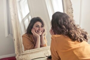 woman smiling wide at her reflection in the mirror