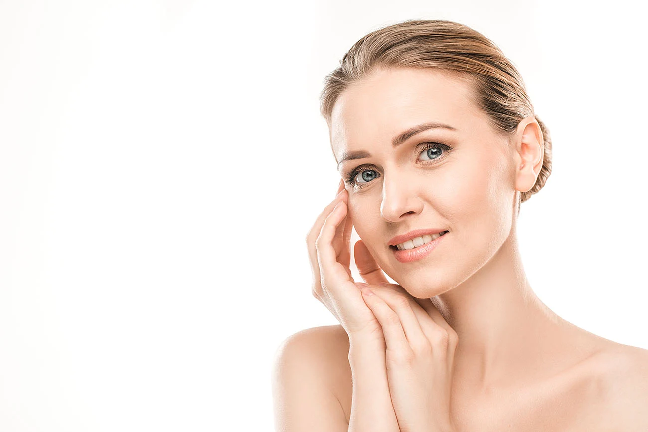 Elegant woman with clear skin touching her face gently on a clean white background.